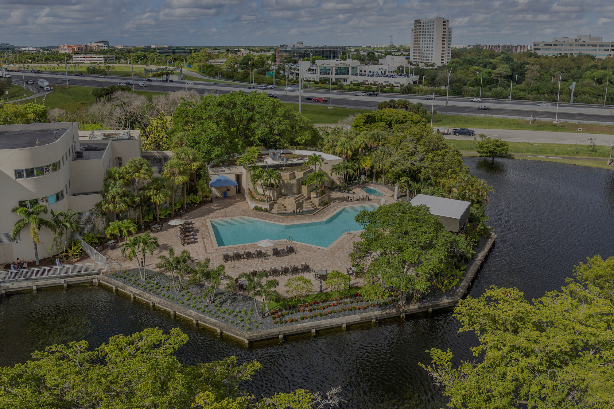 Aerial view of a hotel pool with lots of greenery surrounding it