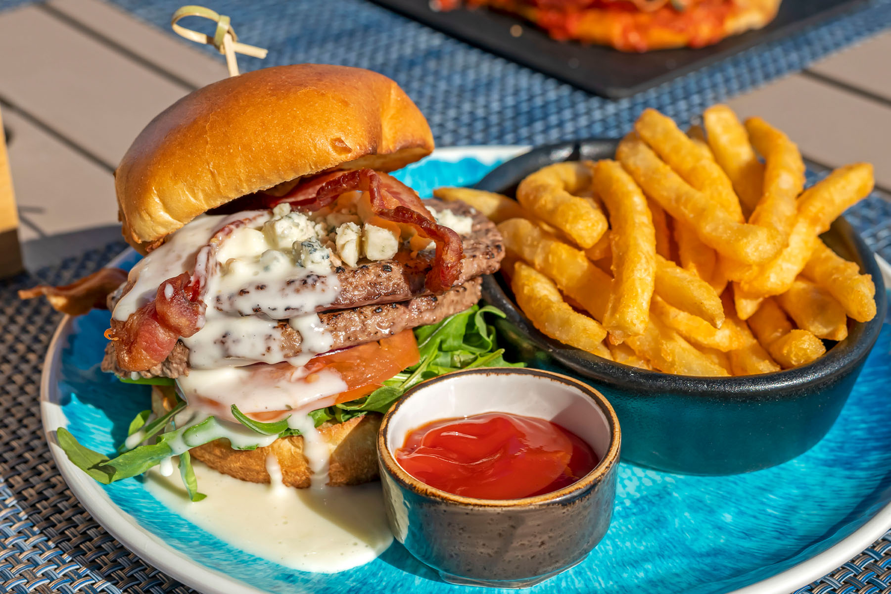 Food photography: A double-burger, a side of ketchup and fries on a blue plate.