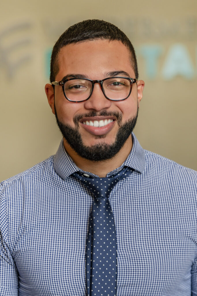 A headshot of a smiling man wearing glasses, a blue shirt and tie.