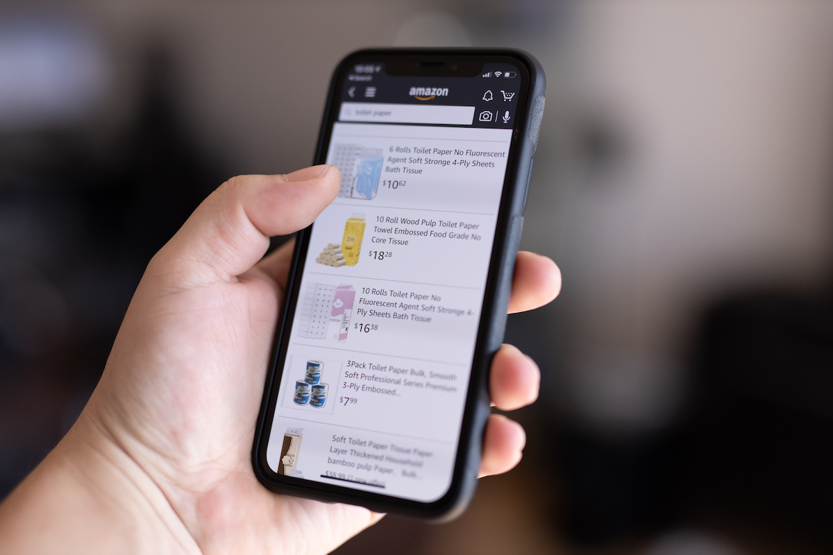 A person holding a phone while scrolling through product listings on Amazon.