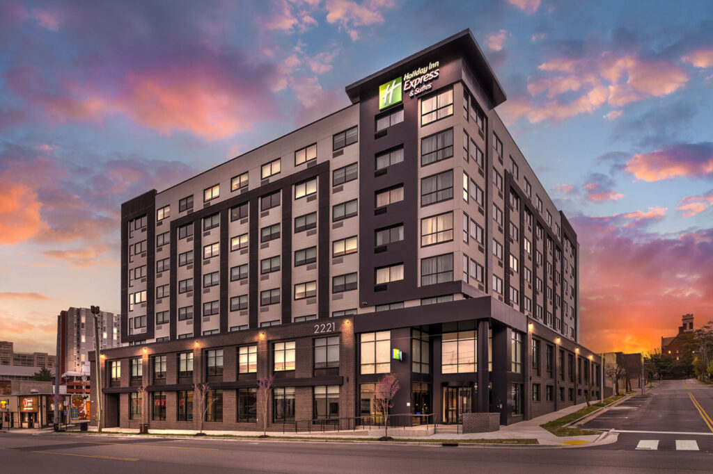 Holiday Inn Express & Suites exterior at twilight, showcasing a multi-story building with illuminated windows against a colorful sunset sky.