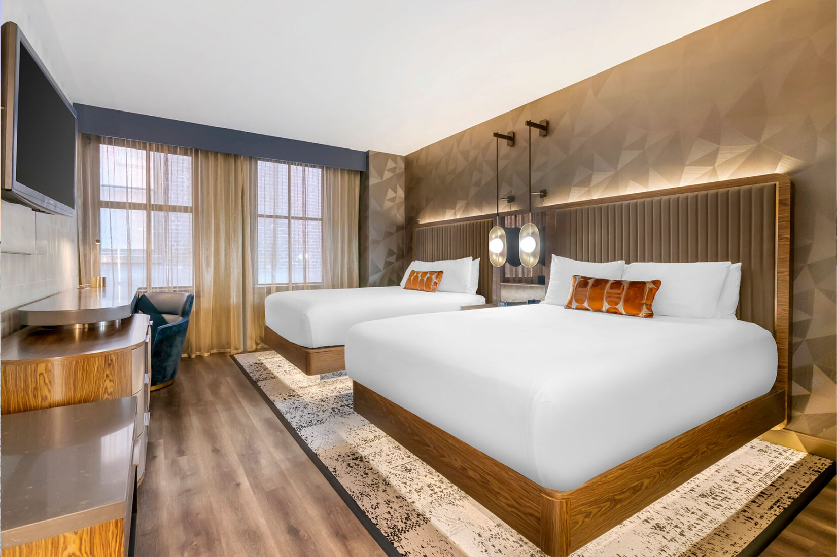 Modern hotel room featuring two queen beds with upholstered headboards, warm accent lighting, large windows with sheer curtains and wood flooring.