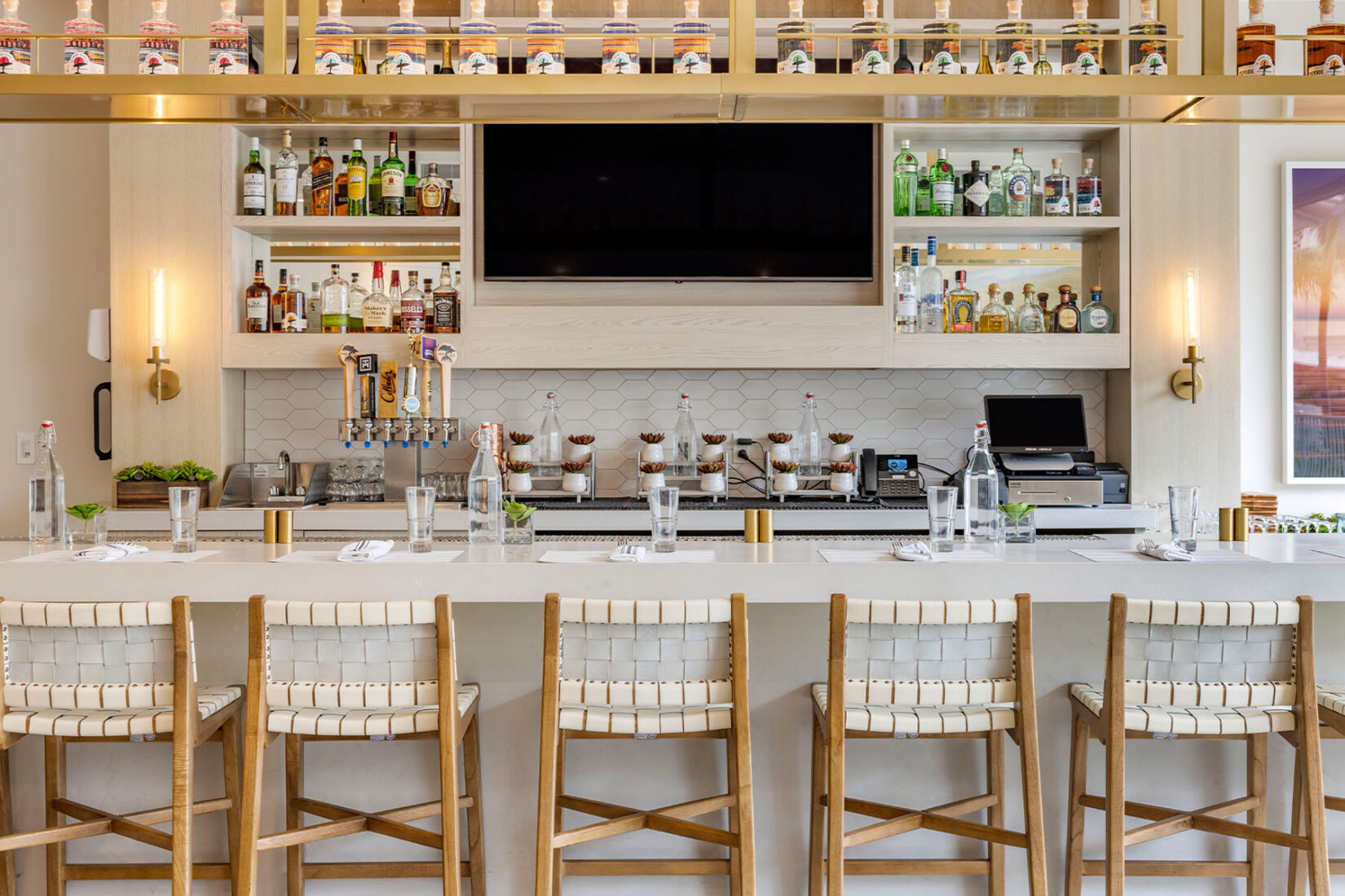 CAF 60 hotel bar with woven stools, backlit liquor shelves, and neatly staged place settings.