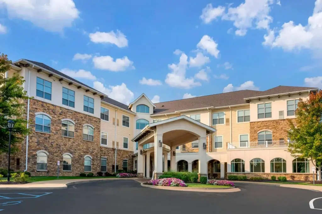 Spanish-style senior living community building with red tile roofs, arched entryways, palm trees and landscaped grounds.